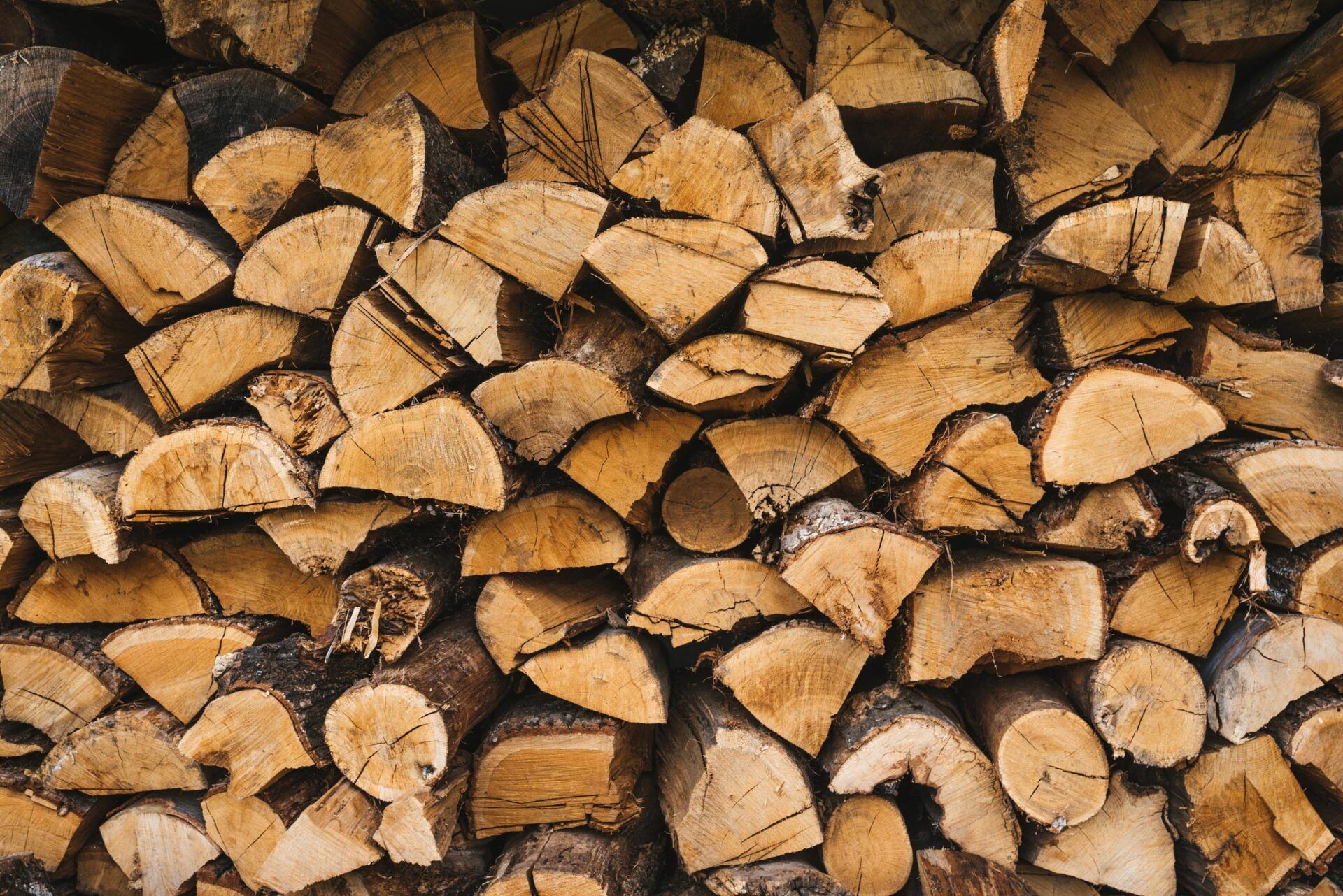 A tightly stacked pile of chopped, light brown firewood logs, showing the textured grain on their cut ends.