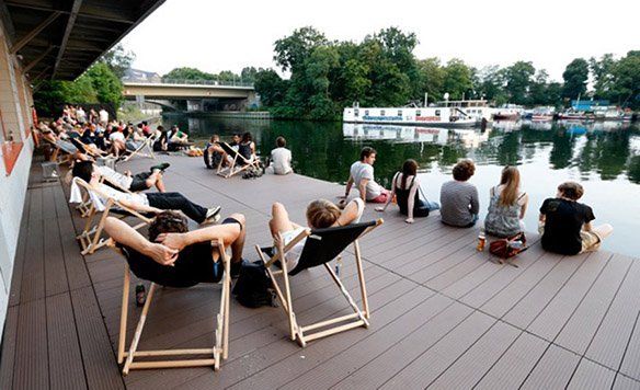 Menschen sitzen in Liegestühlen oder direkt auf dem Bootssteg der Bridge Studios