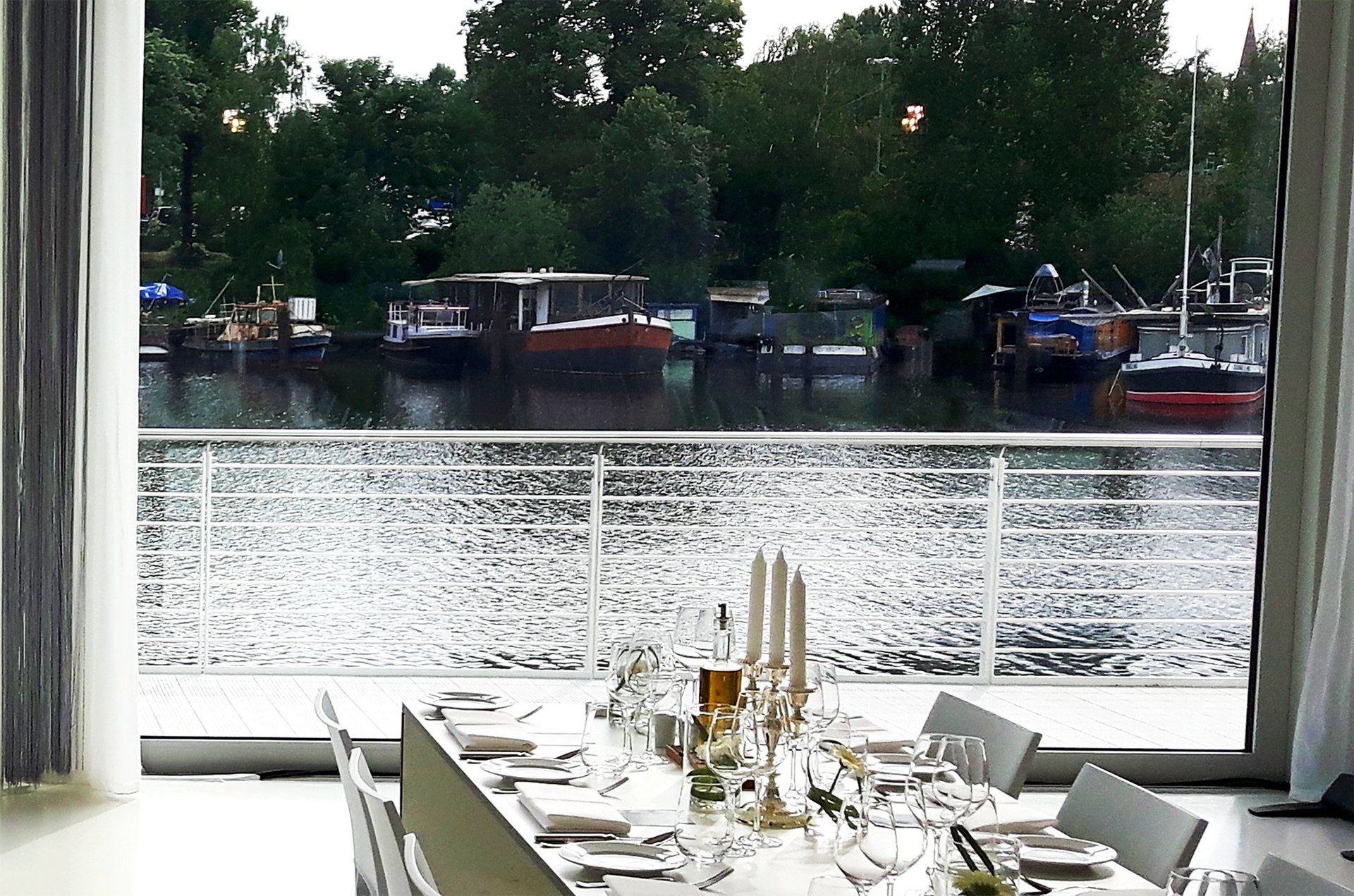 Blick durch die geöffnete Terrassentür von Studio 1 aufs Wasser und Hausboote. Im Anschnitt festlich gedeckte Tafel
