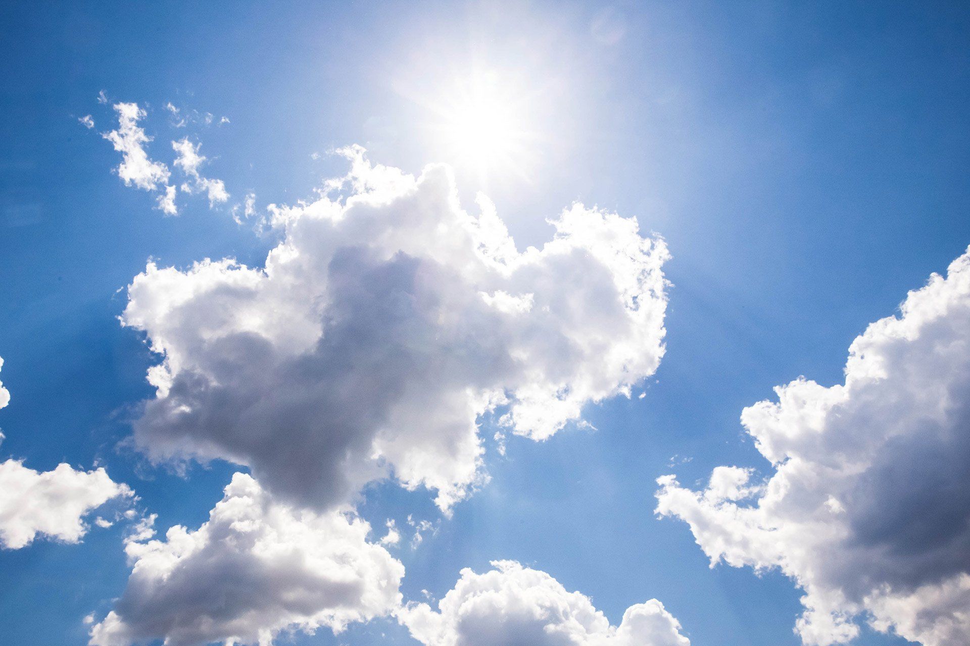 The sun is shining through the clouds in the blue sky.