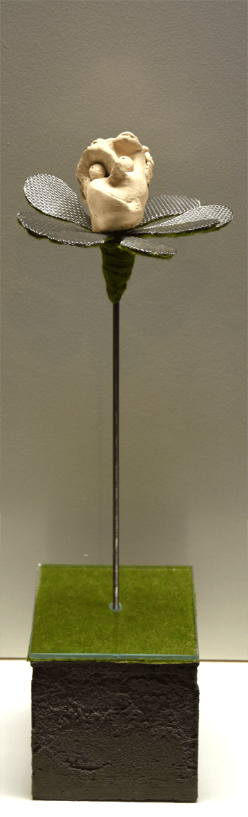 Plastik der Künstlerin Benita von Wendt, die eine Blume darstellt. In der Mitte der metallenen Blütenblätter sitzt ein nachdenklich in die Luft schauender menschlicher Kopf aus Ton. Der metallene Stil der Blume steckt auf einem quadratischen Betonsockel.