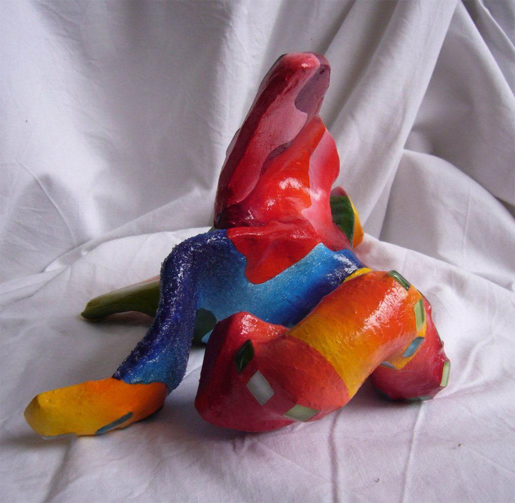 Plastik aus Pappmasché der Künstlerin Benita von Wendt. Titel: Fleur d'espoir 1. Bunte Skulptur die eine kleine vierblätterige Blume, die auf dem Boden liegt darstellt. Die Blume ist mit bunten, abstrakten Ornamenten bemalt und mit Mosaiksteinen besetzt. Rückansicht.