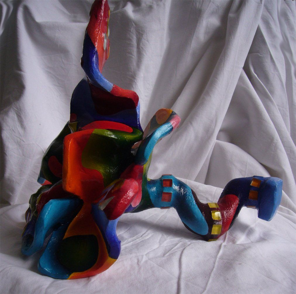 Plastik aus Pappmasché der Künstlerin Benita von Wendt. Titel: Fleur d'espoir 3. Bunte Skulptur die eine kleine sechsblätterige Blume, die auf dem Boden liegt darstellt. Die Blume ist mit bunten, abstrakten Ornamenten bemalt und mit Mosaiksteinen besetzt. Seitenansicht links.