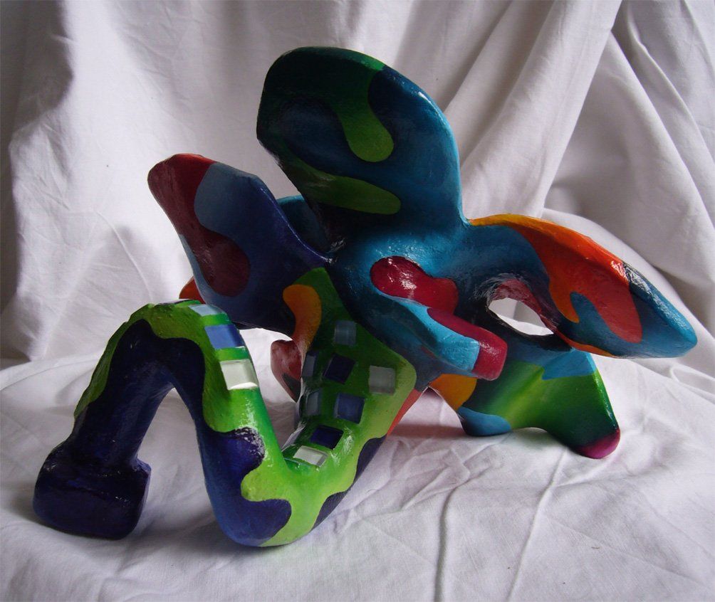 Plastik aus Pappmasché der Künstlerin Benita von Wendt. Titel: Fleur d'espoir 2. Bunte Skulptur die eine kleine sechsblätterige Blume, die auf dem Boden liegt darstellt. Die Blume ist mit bunten, abstrakten Ornamenten bemalt und mit Mosaiksteinen besetzt. Rückansicht.