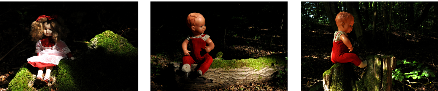 Fotografie der Künstlerin Benita von Wendt. Titel: Stumm. Die Fotografie zeigt 2 identische männliche und 1 weibliche altmodische Puppe die auf Baumstämmen oder Steinen sitzen, ein Spiel aus Licht und Schatten setzt die Puppen in Szene, die Umgebung löst sich in der Dunkelheit auf. Die Fotoarbeit besteht aus 3 Fotografien die miteinander in Beziehung stehen.