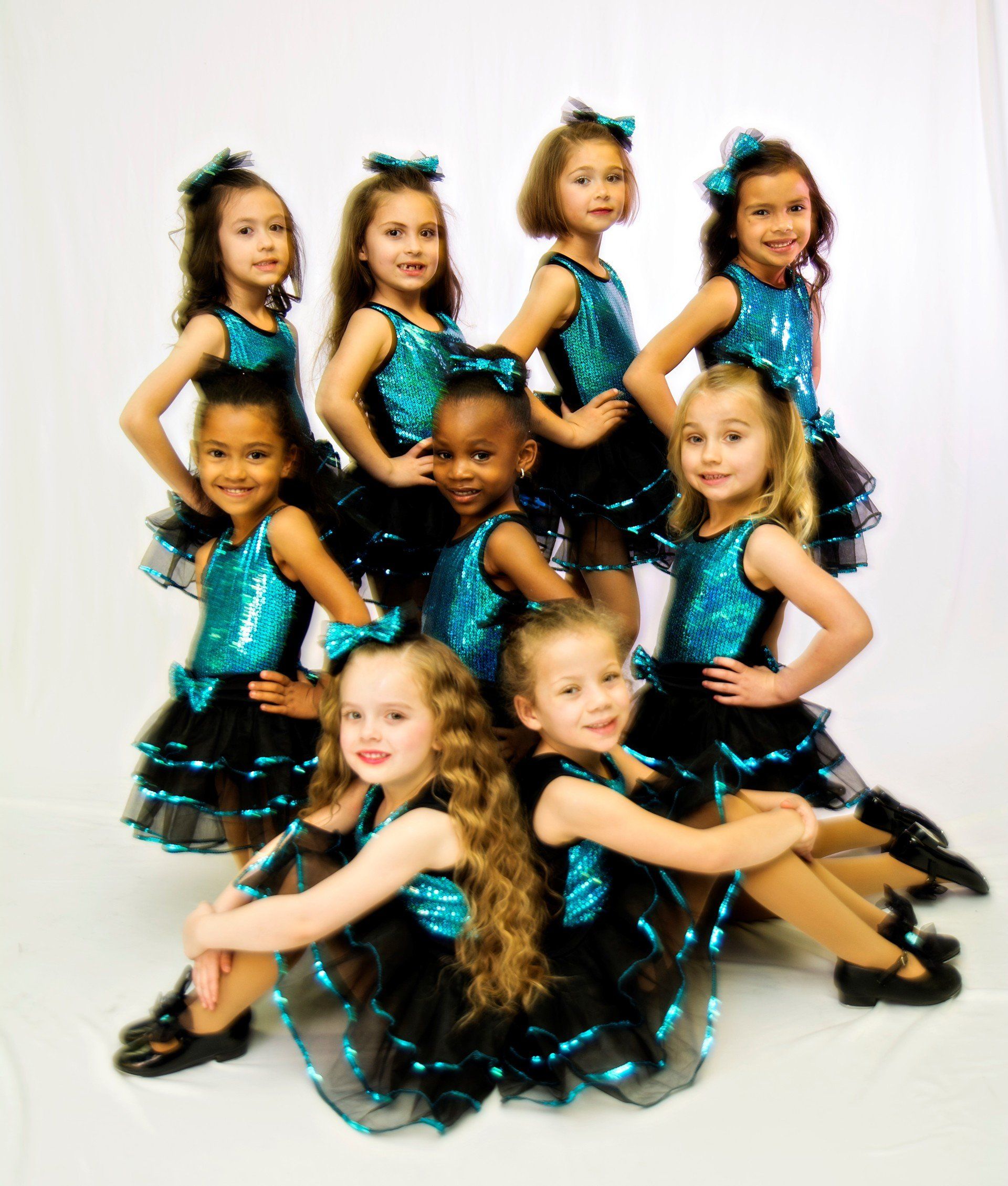 Group of young girls in turquoise and black dance costumes posing for a studio photo.