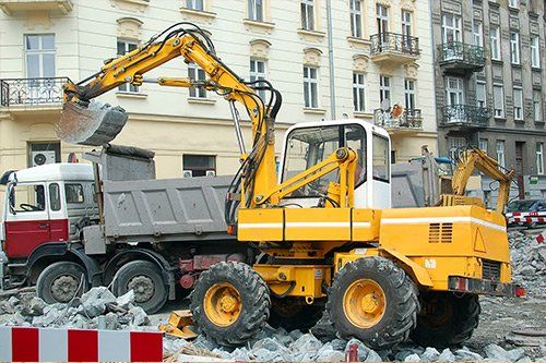 una ruspa gialla e un camion da lavoro in una strada di citta’ e vista delle macerie