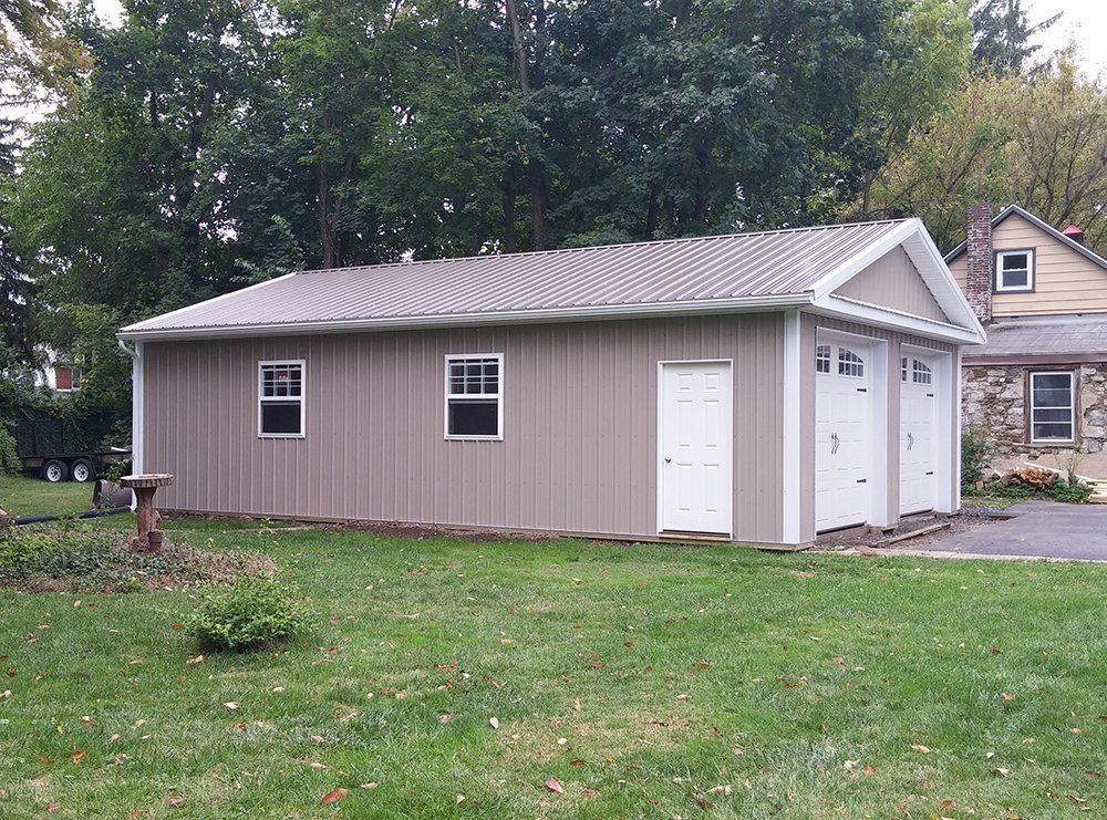 A brown garage with white doors and windows in front of a house