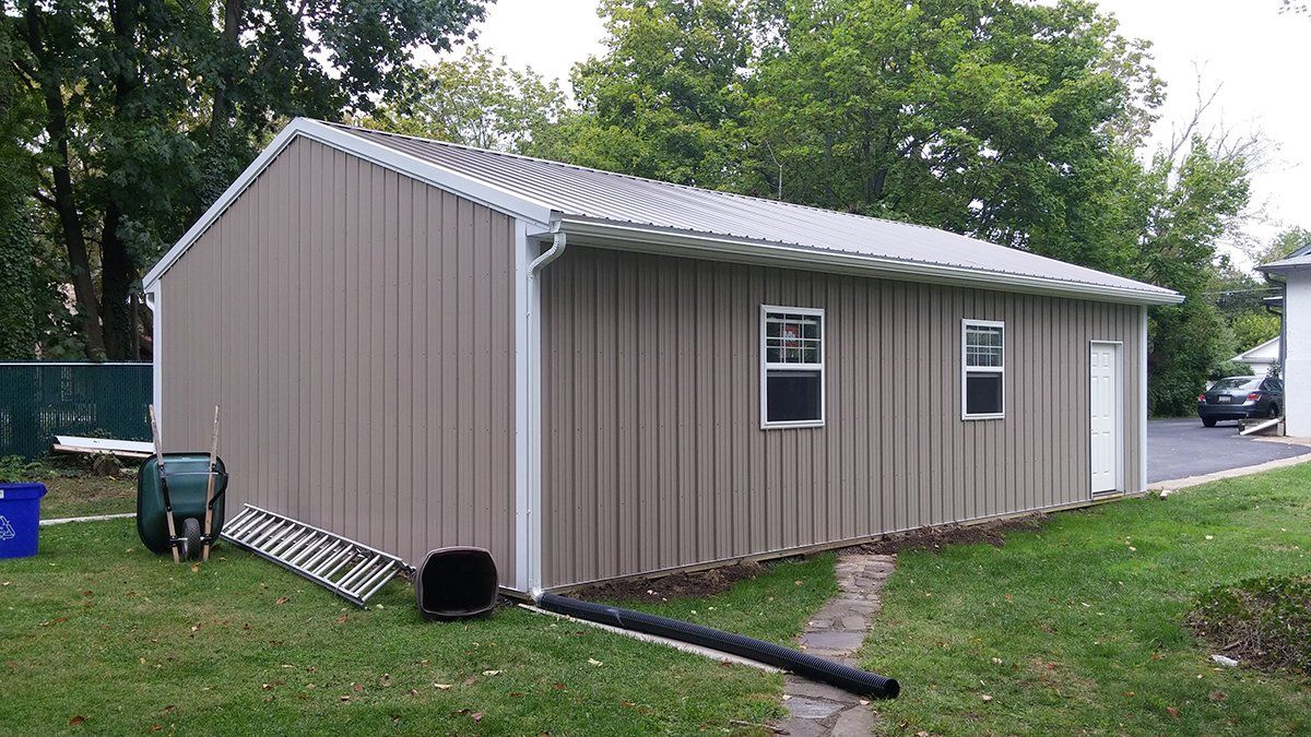 A large metal building with a white roof is in the backyard of a house.
