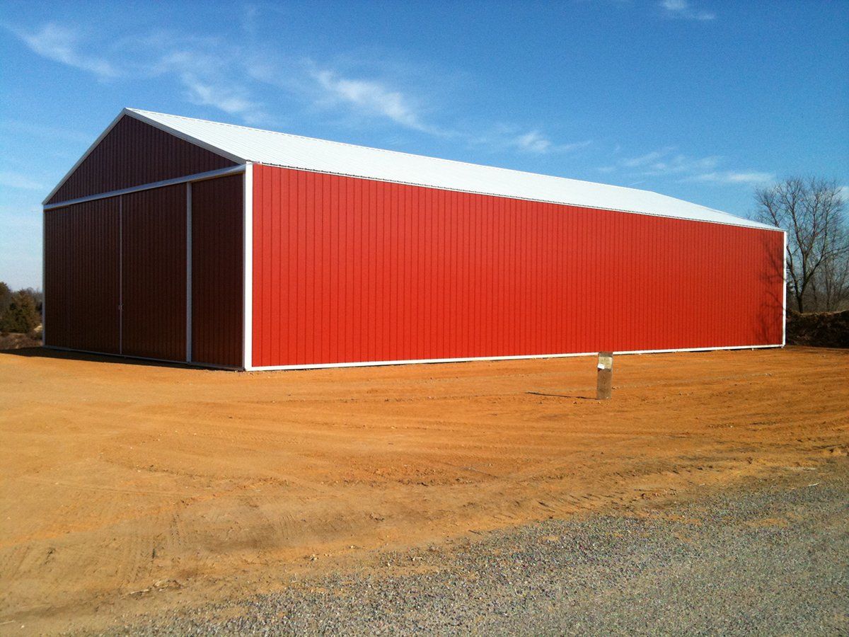 A large red barn with a white roof is in a dirt field