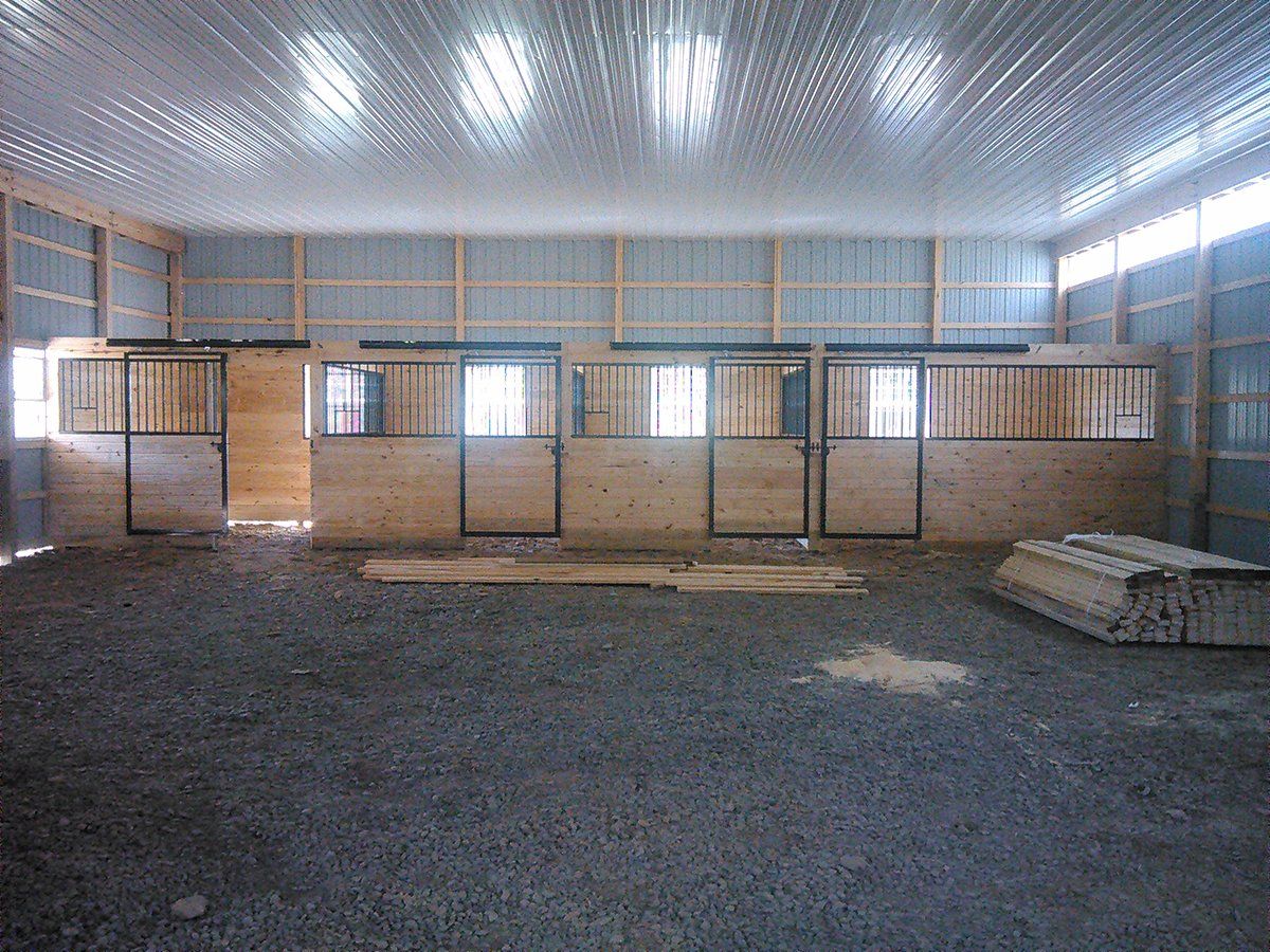 A large empty barn with wooden stalls and a gravel floor.