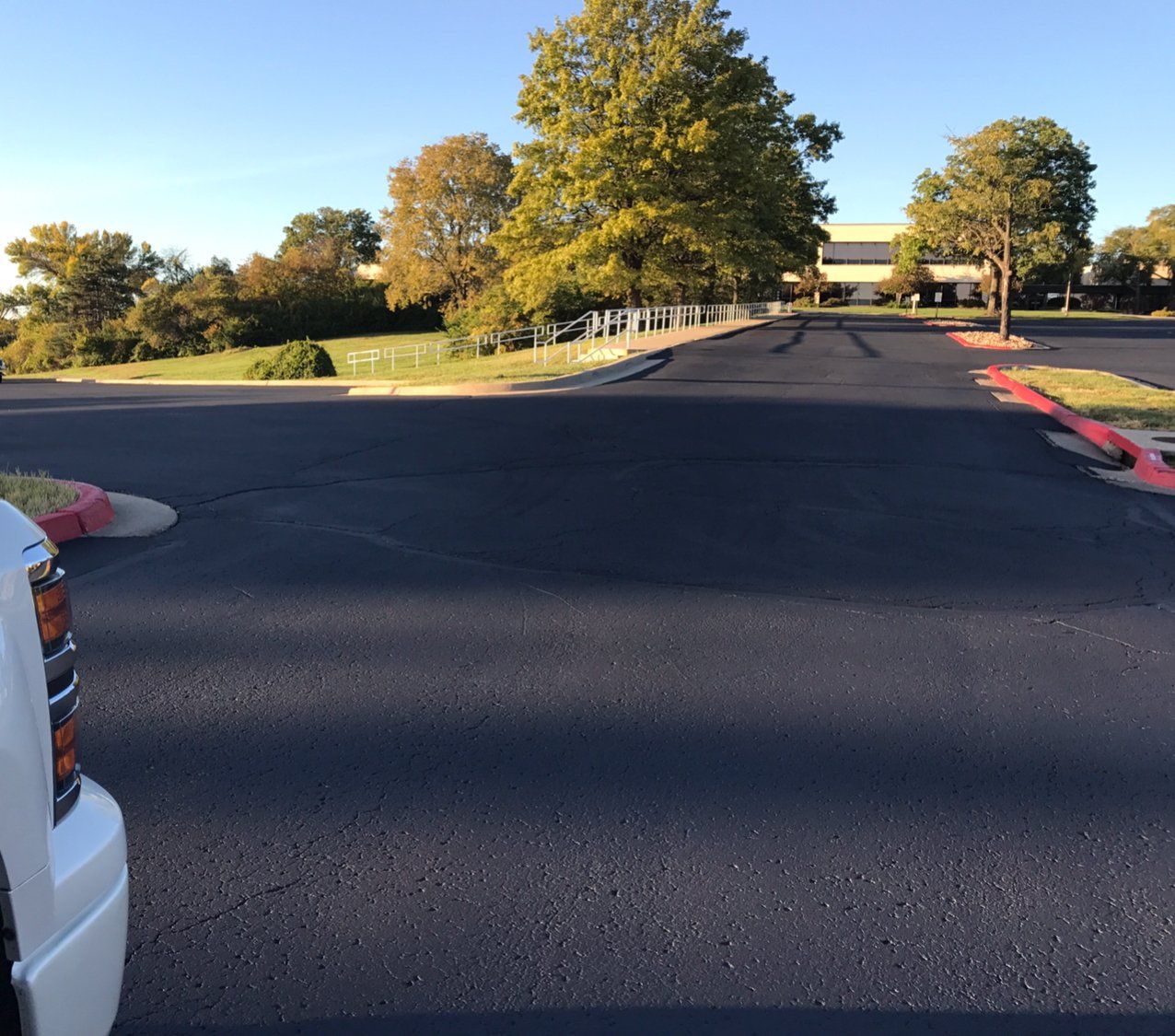 Empty parking lot with trees and a building in the distance at sunset