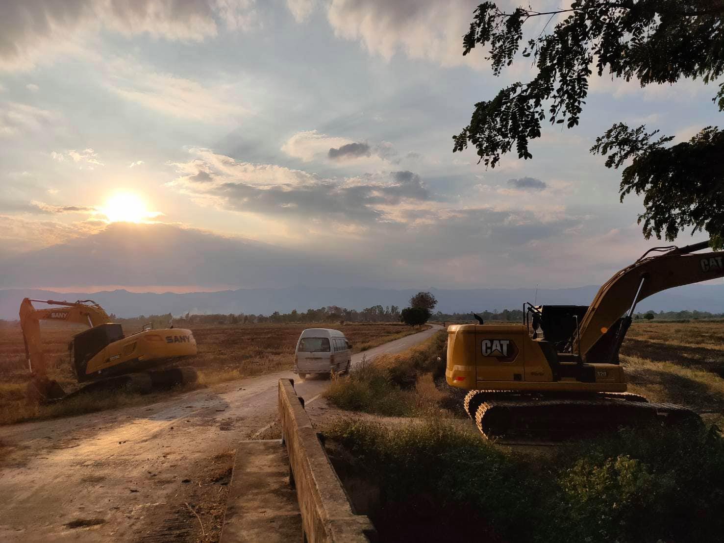 Sunset over a dirt road construction site with two excavators and a small truck