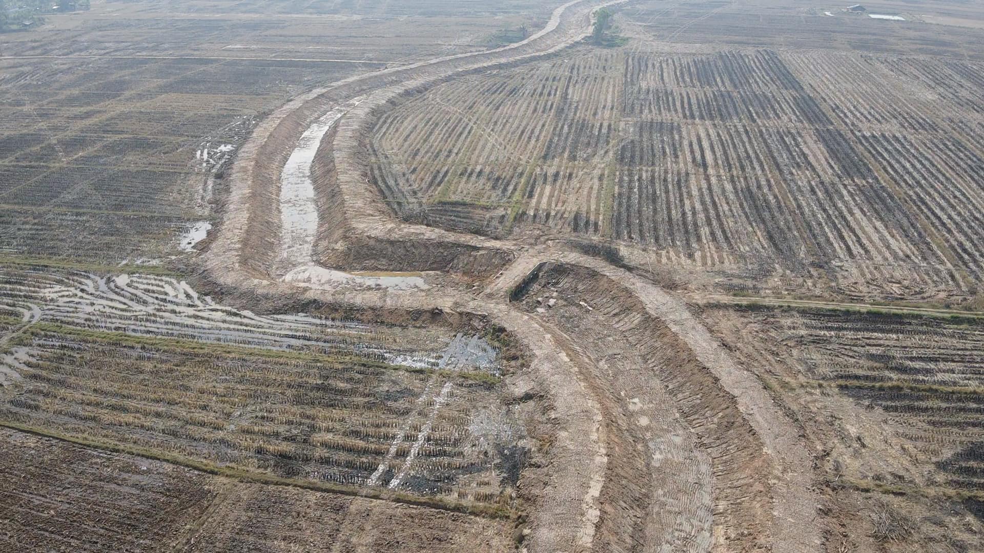 Aerial view of a wide dirt road cutting through a barren, plowed field