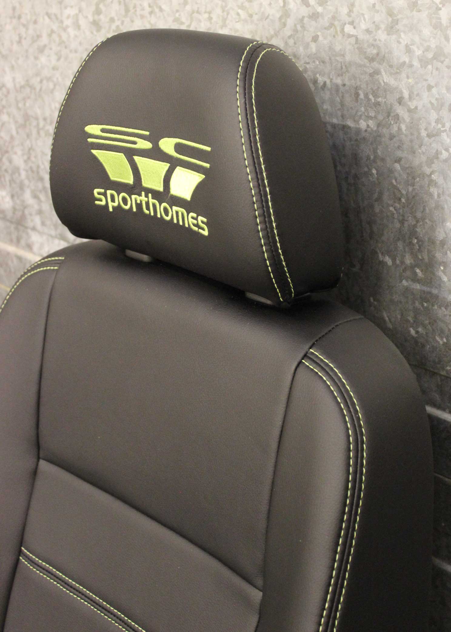 A black car seat with the sporthomes logo on its headrest.