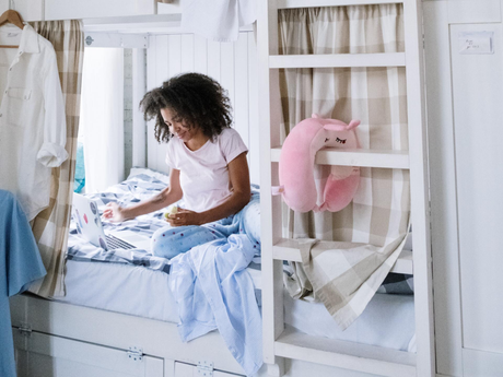 a woman is sitting on a bunk bed using a laptop .