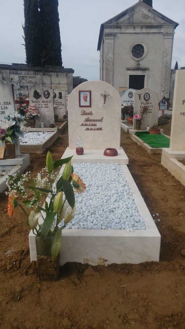 Una tomba in un cimitero con fiori e un edificio sullo sfondo.
