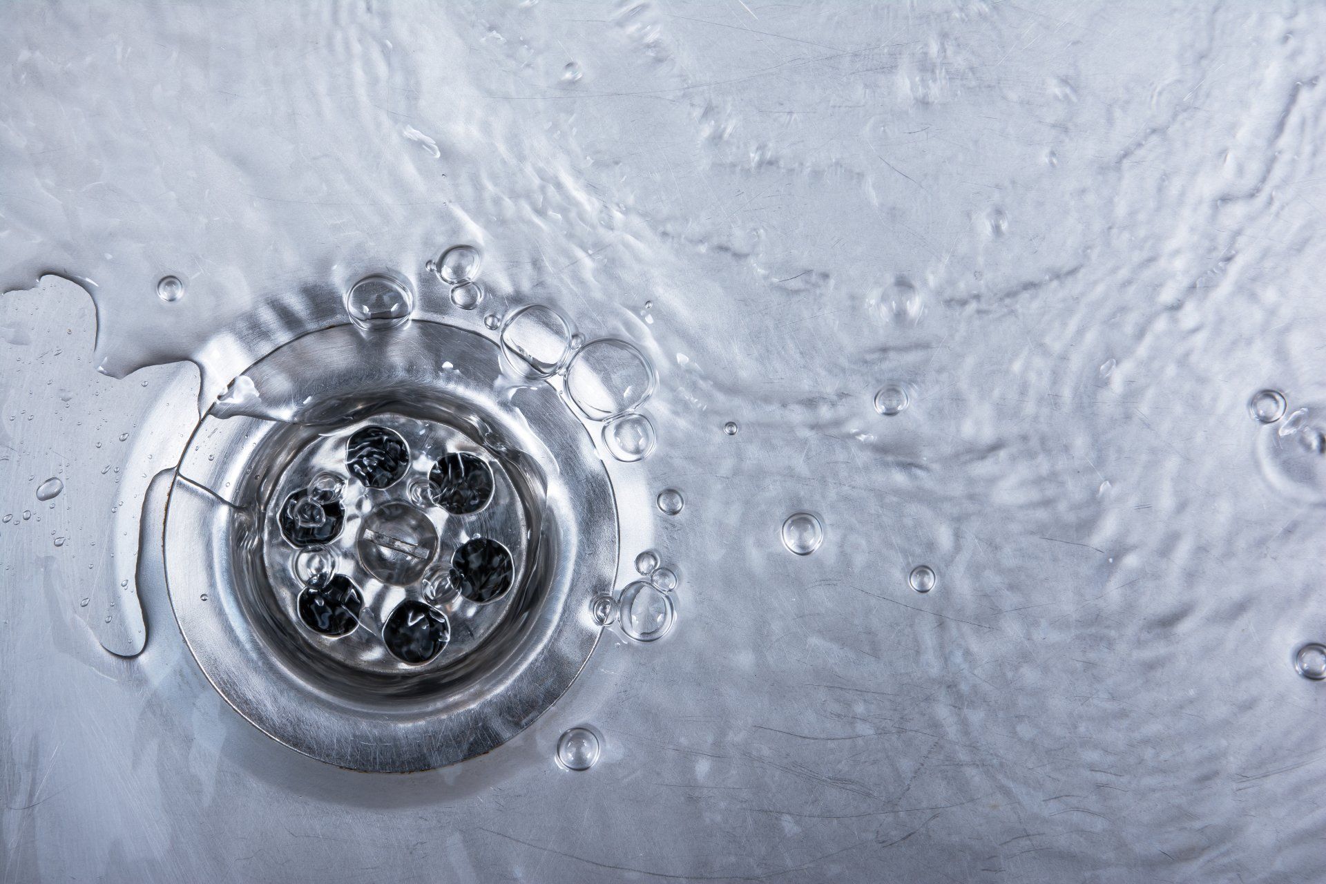Water flowing into a shiny metal sink drain. Water flowing into a shiny metal sink drain.