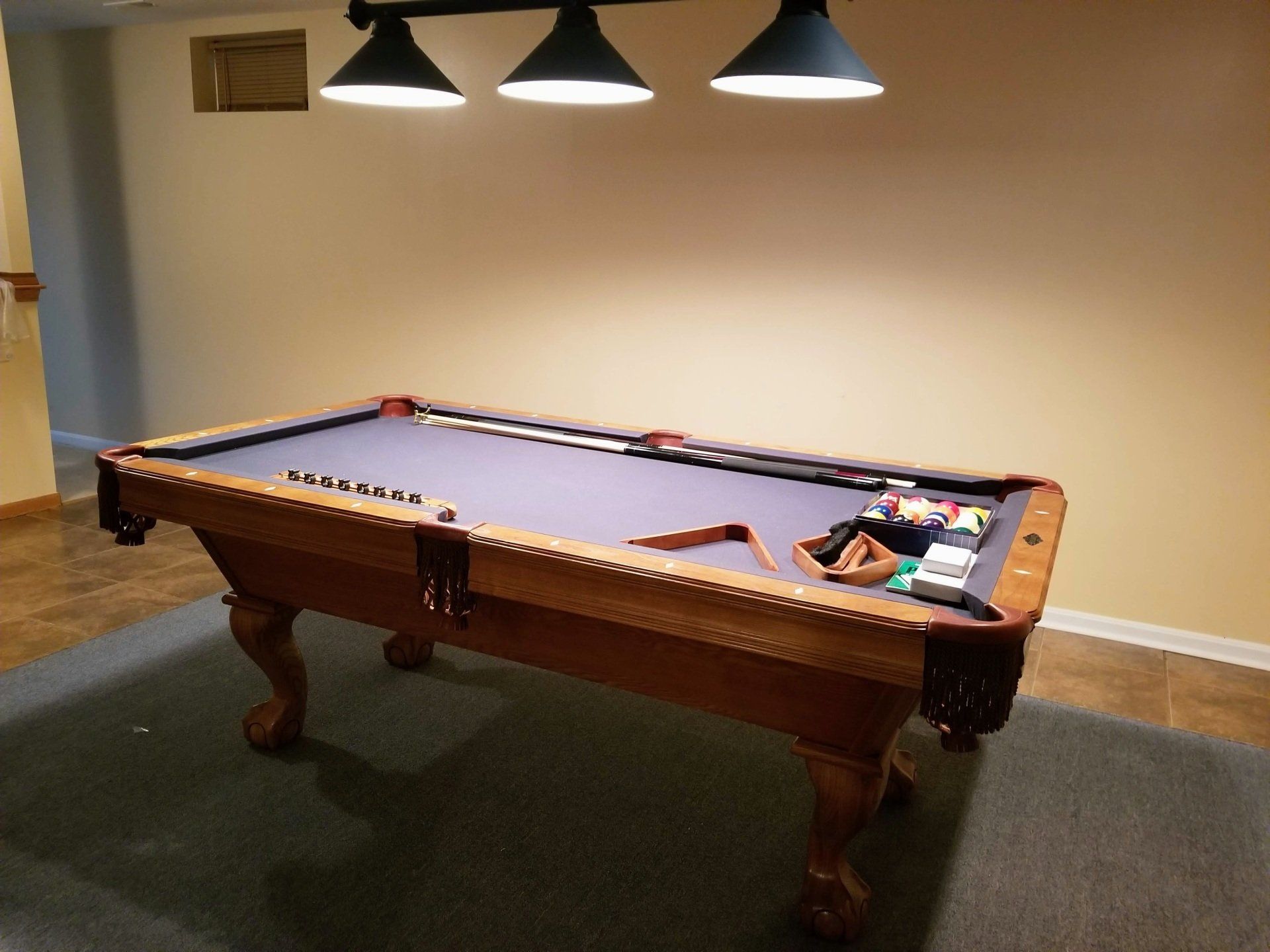 A pool table is sitting in a room with three lights hanging from the ceiling.