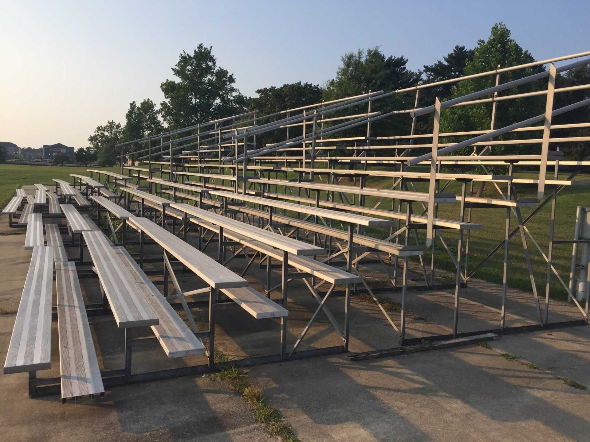 A row of white benches in a stadium with trees in the background