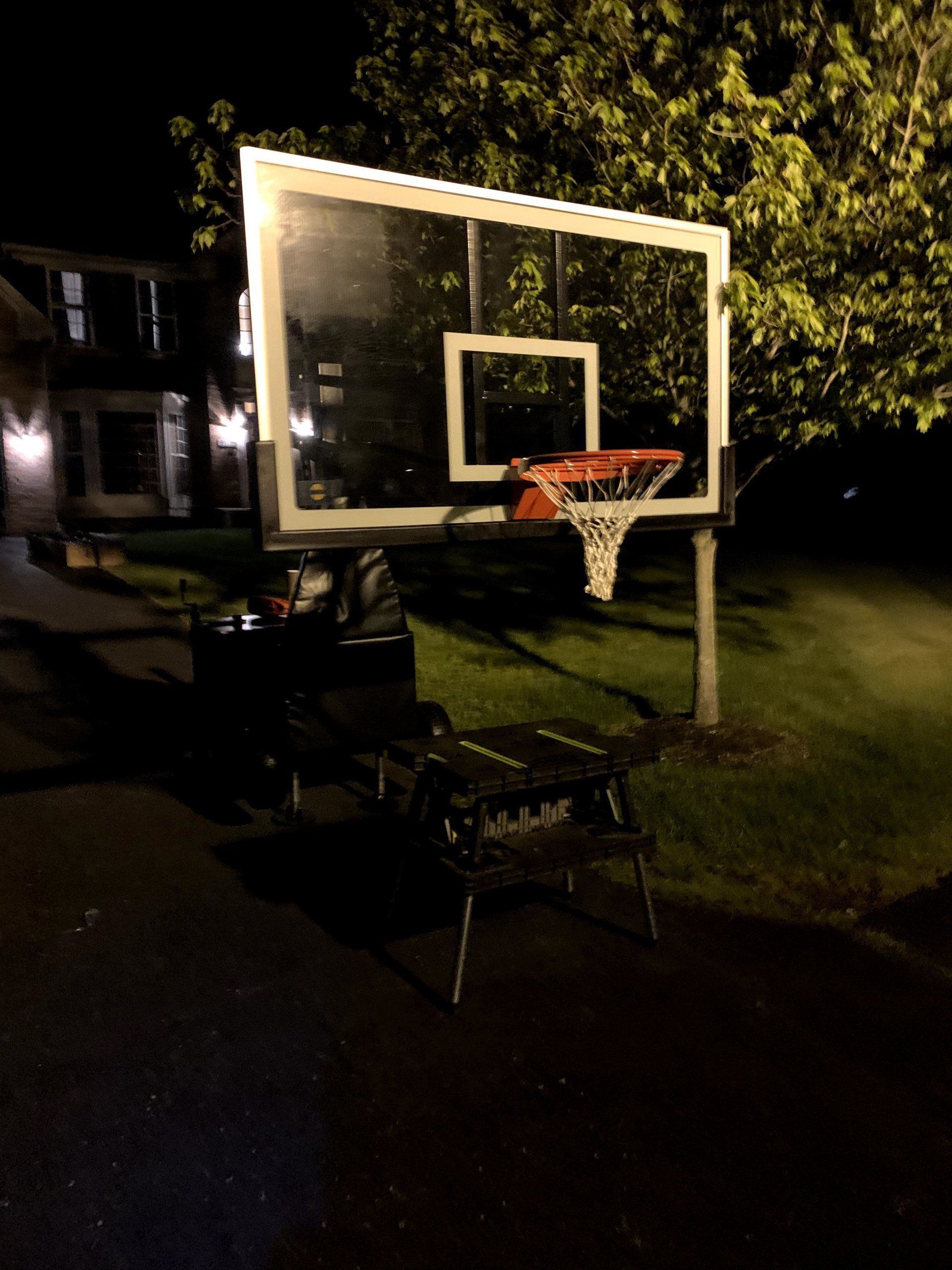 A basketball hoop is lit up at night in front of a house