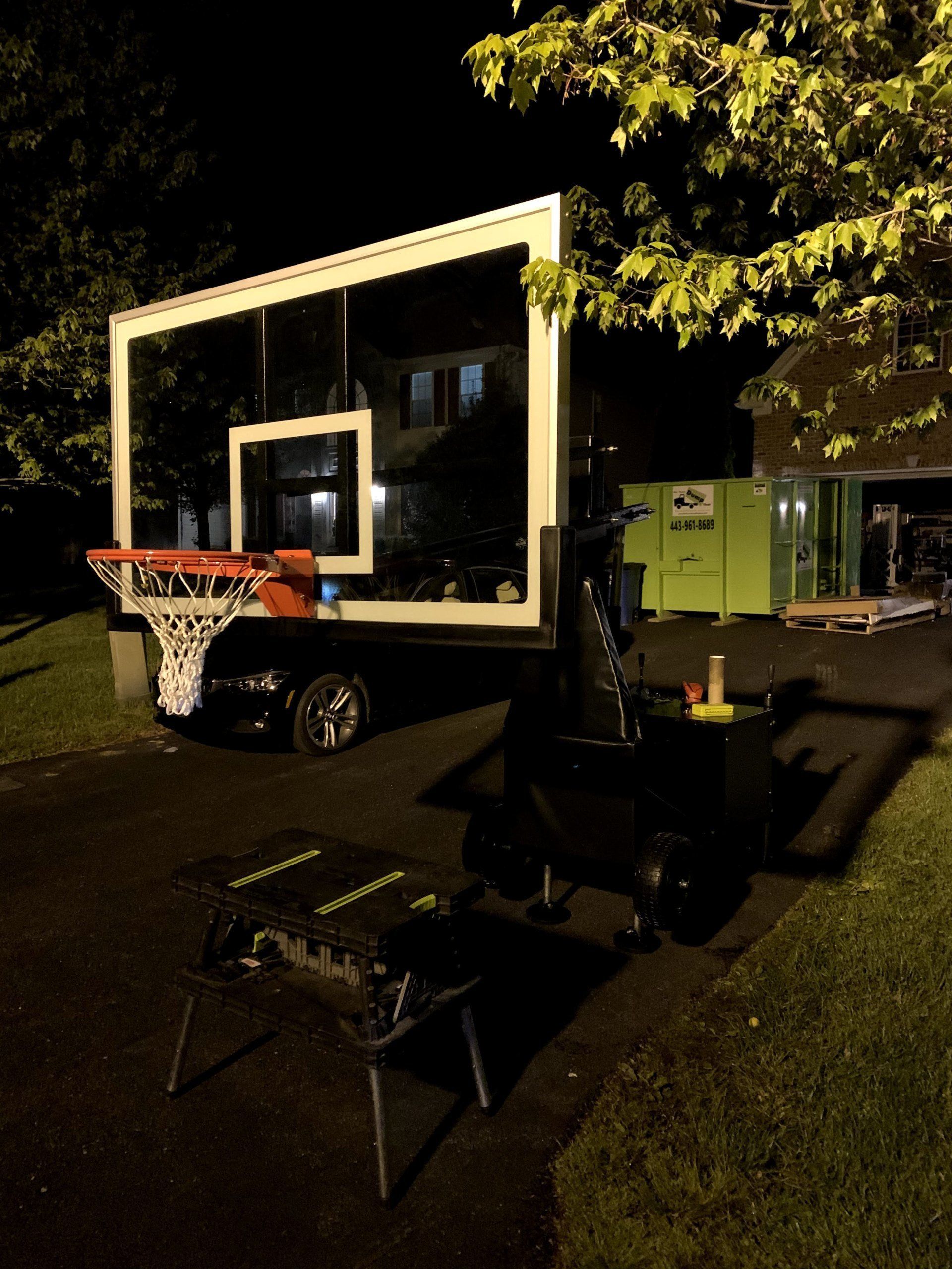 A basketball hoop is parked in front of a house at night.