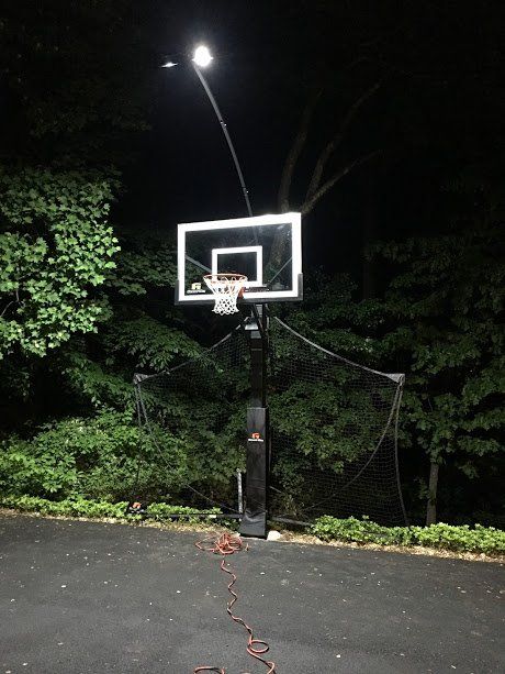 A basketball hoop is lit up at night with trees in the background.