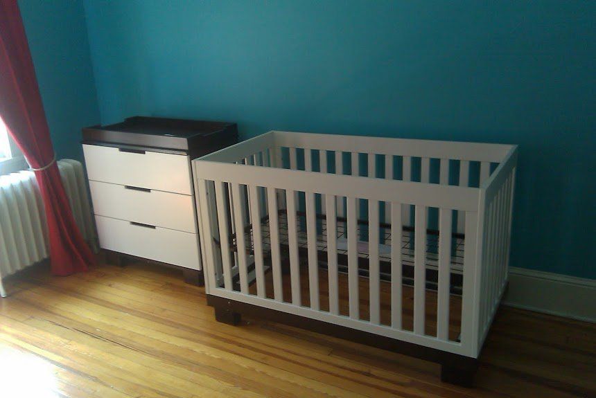 A crib and dresser are in a room with blue walls.