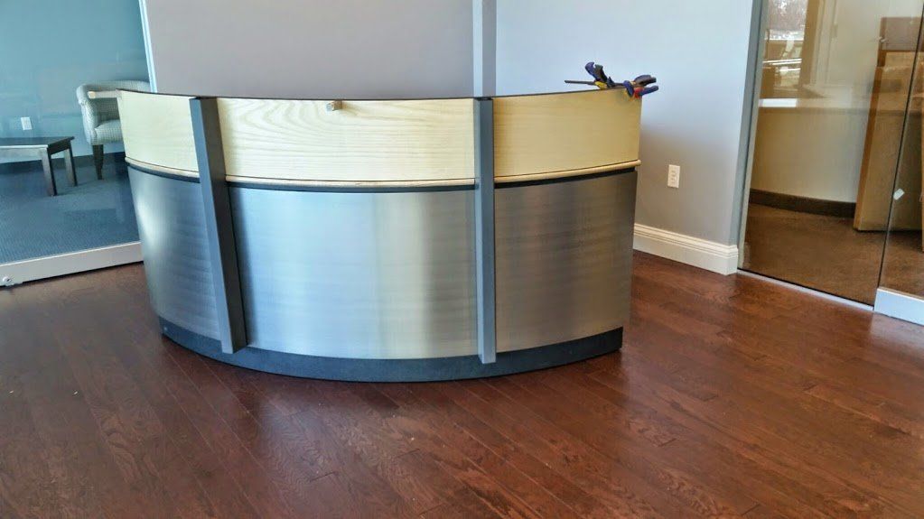 A stainless steel and wooden reception desk in a room with hardwood floors.