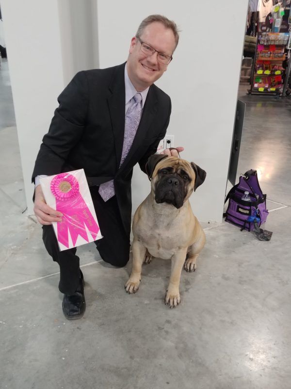 A person posing with a large dog at what appears to be a dog show.
