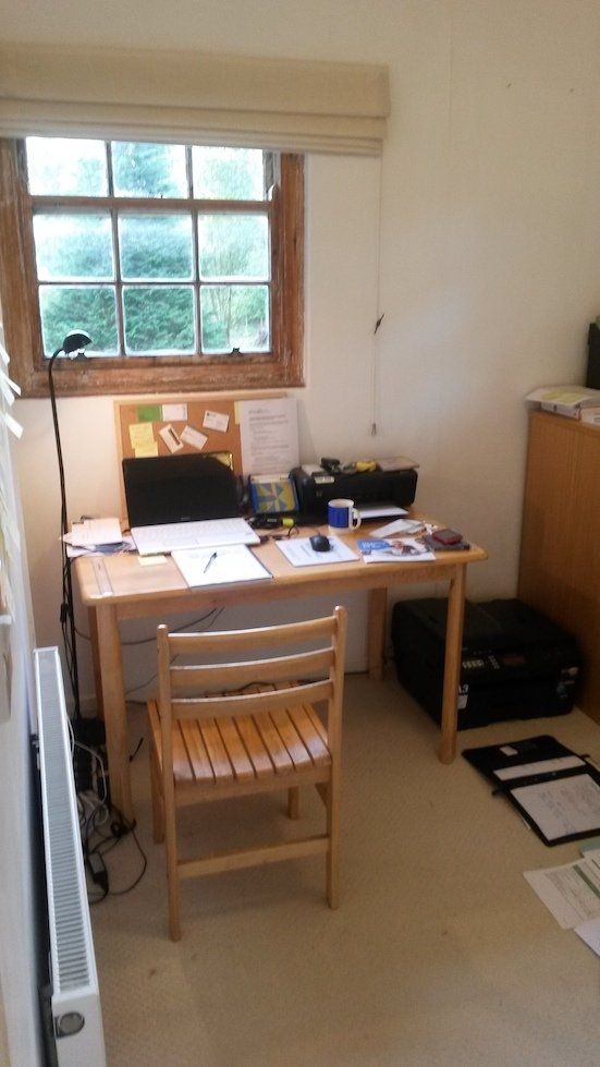Small home office with a desk, chair, laptop, papers, and a window above the workspace.
