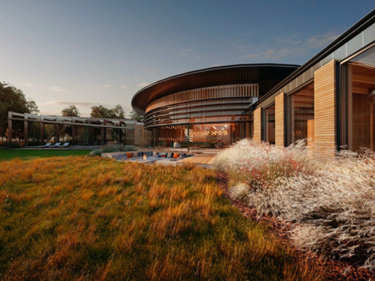 Modern building with curved glass facade, surrounded by tall grass and landscaped shrubs at sunset
