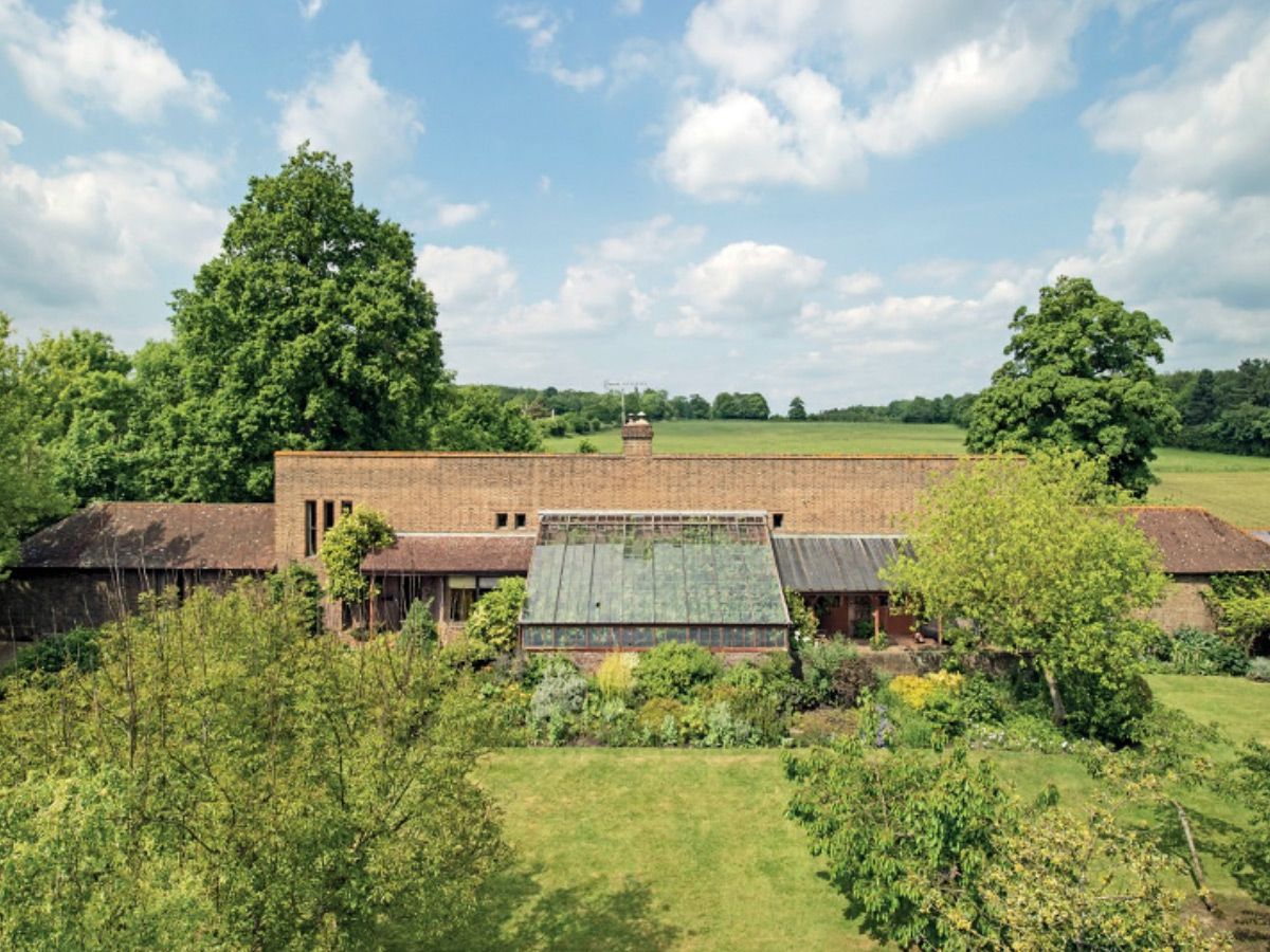 Countryside farmhouse with thatched roofs, surrounded by green fields and trees under a blue sky