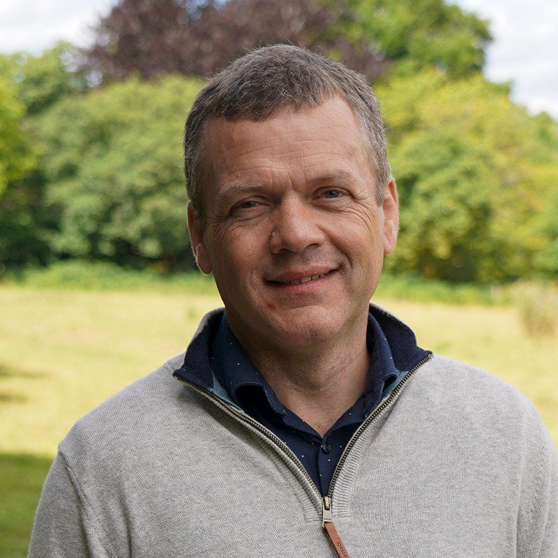 Smiling man in a gray sweater standing outdoors in a green park