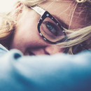 Close-up of a smiling face with black glasses, lying on a blue blanket