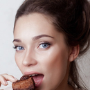Woman with blue eyes eating a brownie, close-up portrait against a light background