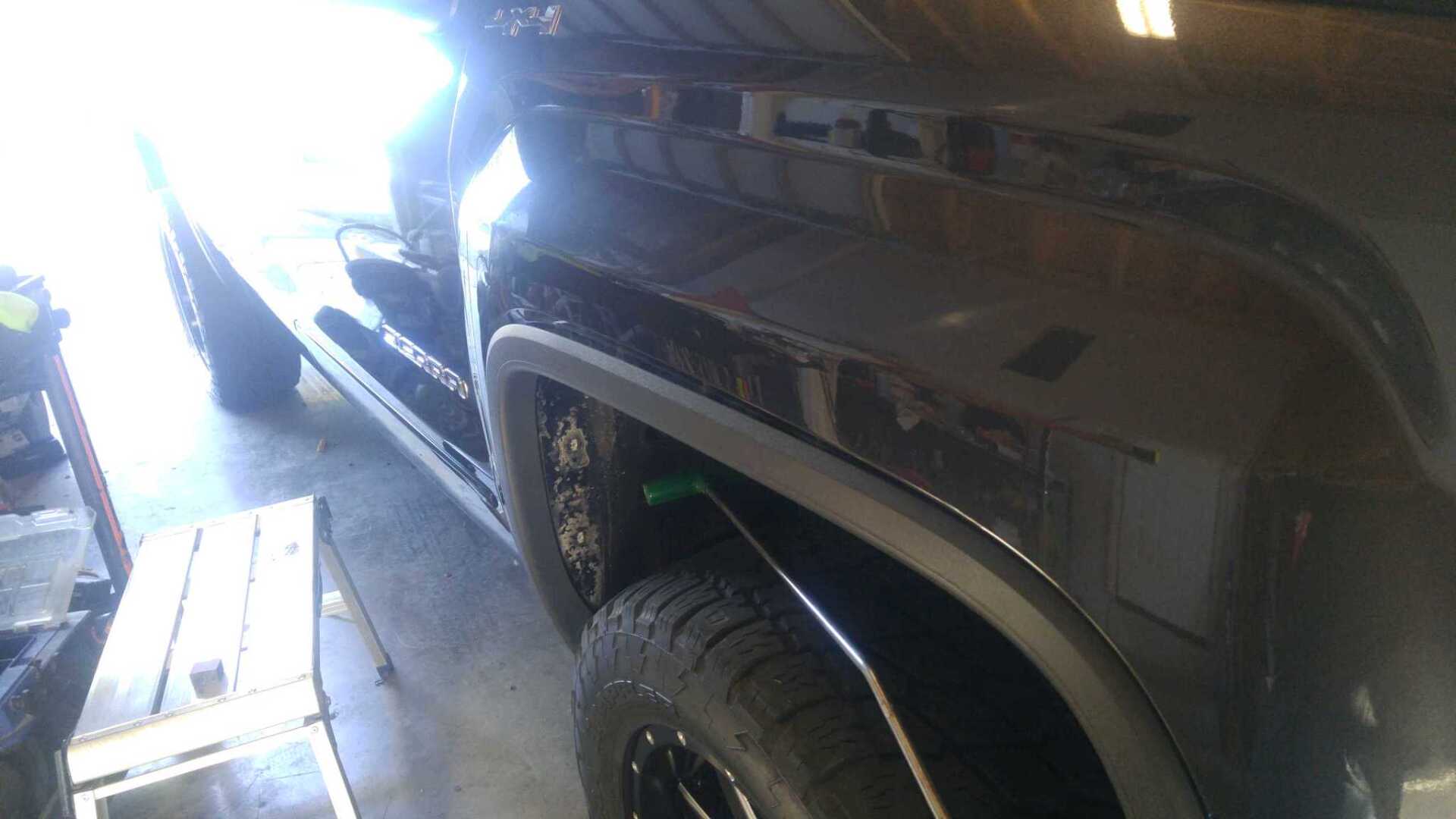 Black pickup truck parked in a garage, viewed from the side near the front wheel.