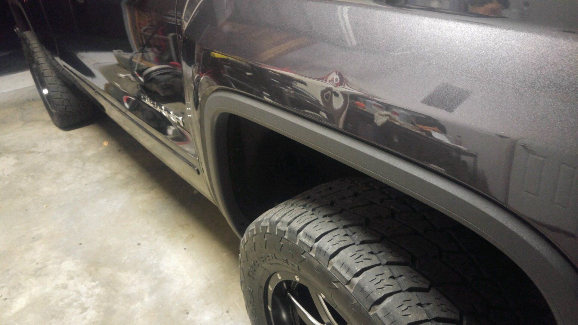 Gray pickup truck side with black wheel and tire parked on a concrete floor, low-angle close-up