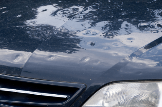 Close-up of a dark car hood and windshield with raindrops and a headlight visible
