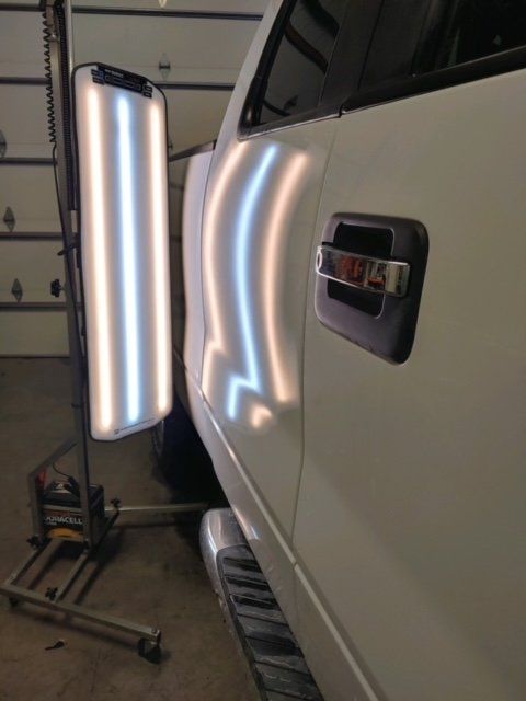 White pickup truck door being inspected with a bright vertical light in a garage workshop