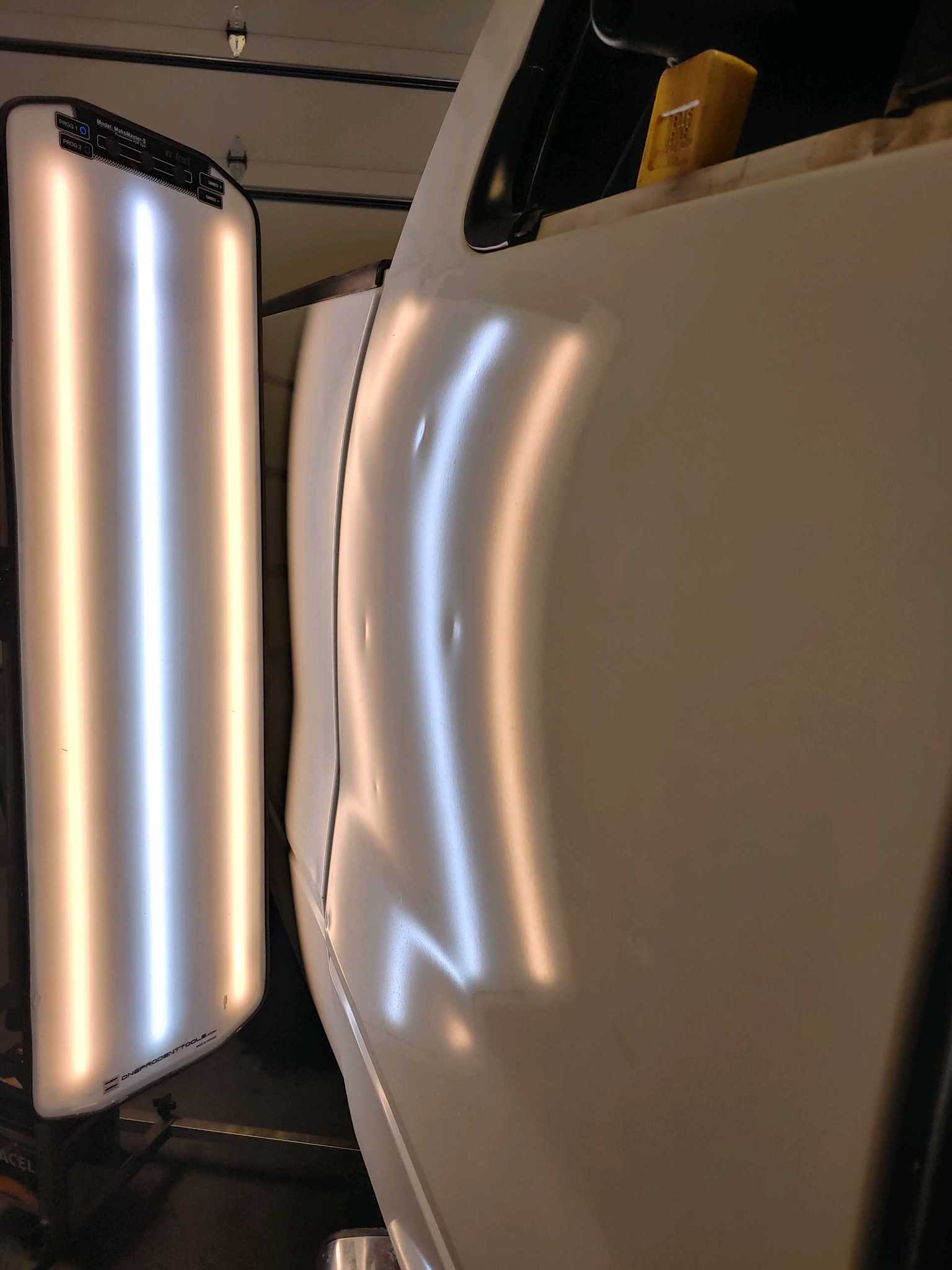 Close-up of a glossy white car body beside a bright light panel in a garage or studio.