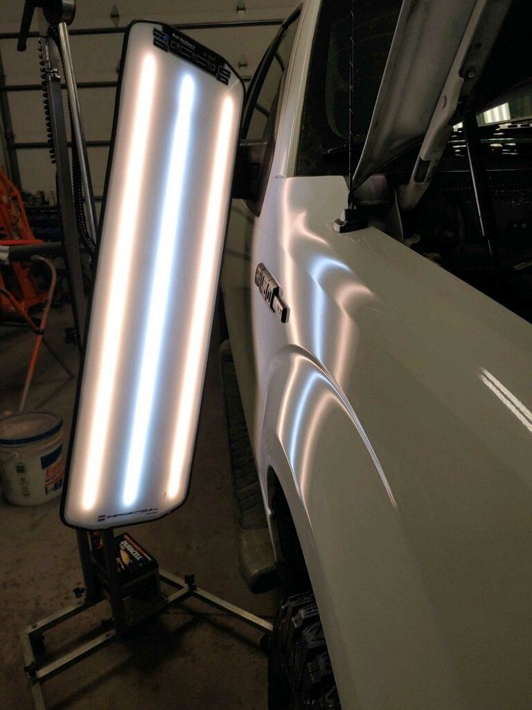 Tall light panel illuminating the glossy side of a white car in a workshop garage