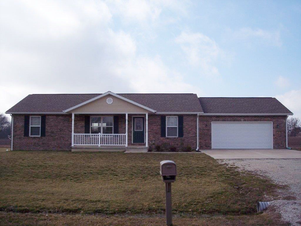 Single-story brick house with a front porch, white garage, and mailbox by the driveway under a cloudy sky.