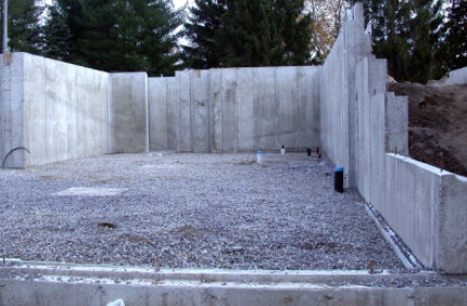 Concrete foundation with gravel floor, retaining walls, and wooded hillside in the background