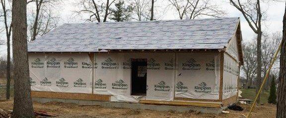 Partially built house wrapped in white housewrap in a wooded yard