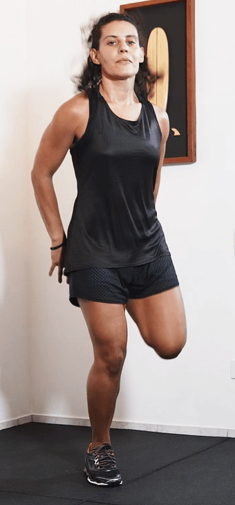 Uma mulher de camiseta preta e shorts está apoiada em uma perna só.