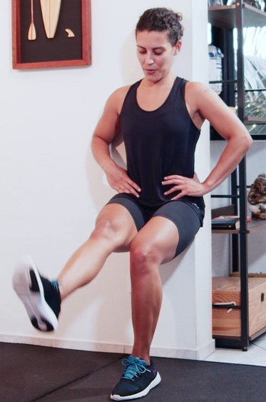 Uma mulher está agachada em uma parede com uma perna para cima