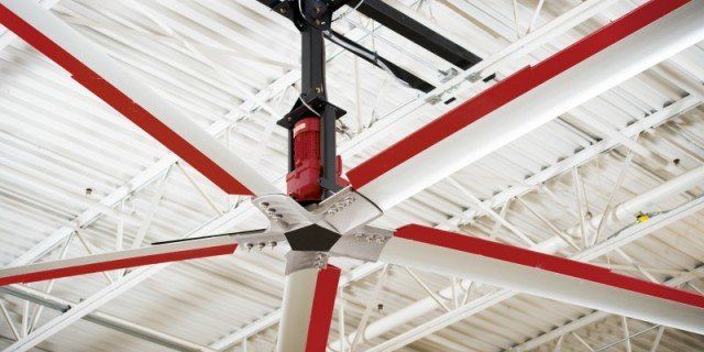 A ceiling fan with red and white blades is hanging from the ceiling of a building.