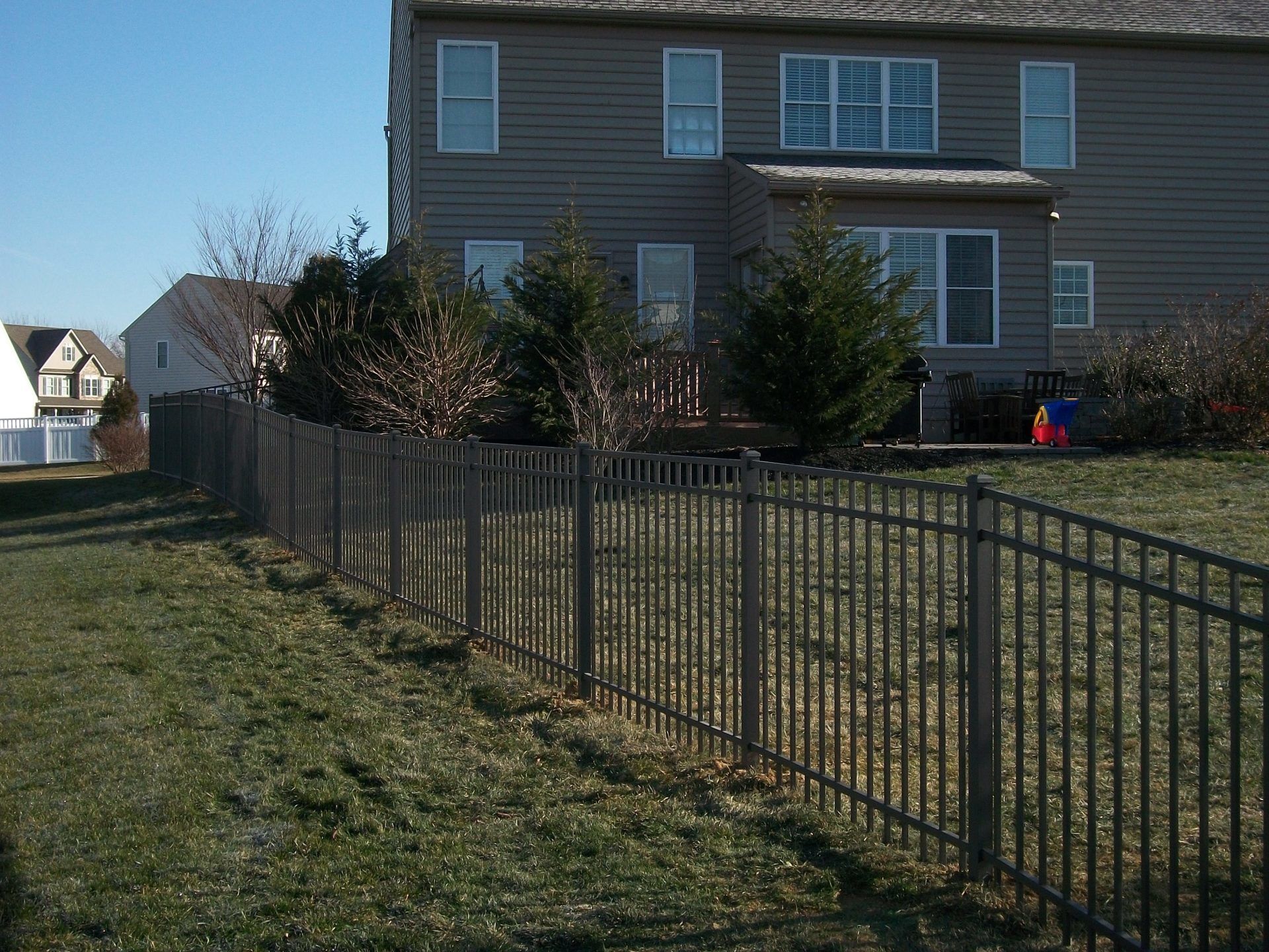 Black metal fence in a backyard, with a house in the background. Green grass and blue sky.