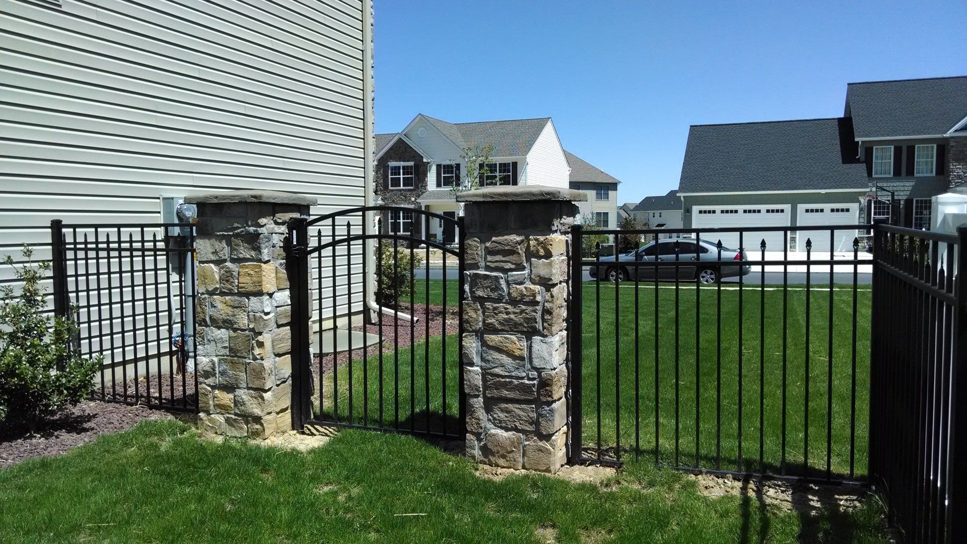 Black metal fence with stone pillars and gate, green lawn, houses in the background in Lancaster, PA.